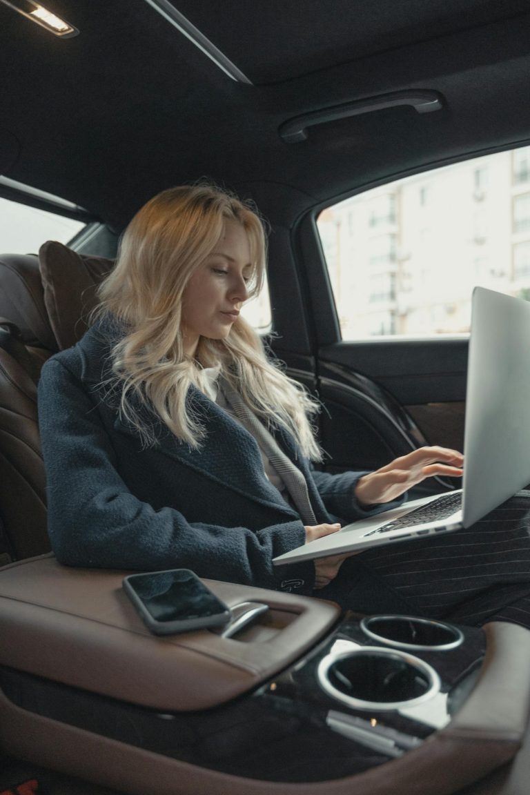 Businesswoman working remotely on a laptop in the backseat of a luxury car. Stylish, modern, and focused.